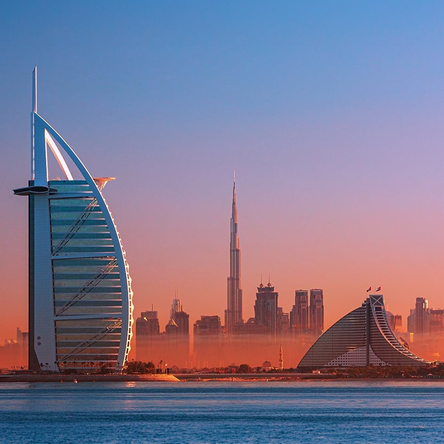 Dubai skyline at sunset with iconic buildings and a calm sea.