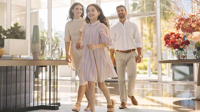 Happy family walking through a bright modern hotel lobby with floral arrangements and large windows