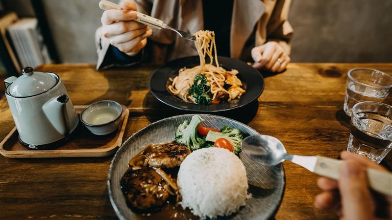 Person eating noodles and rice dishes at a restaurant table